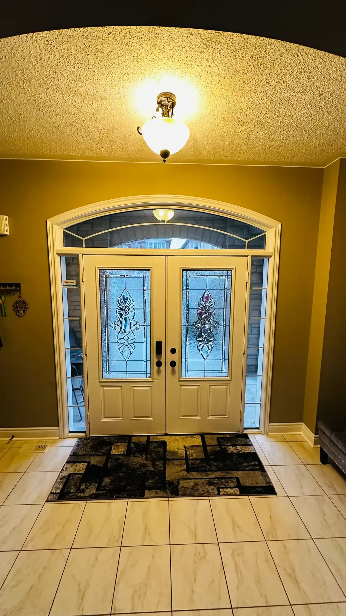 White double front doors with decorative glass and arched transom inside a Barrie foyer
